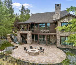 Back of house featuring a patio, stone siding, a balcony, a fire pit, and a stairway to an upper patio & the covered deck
