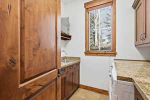 Main floor laundry room featuring granite counters, a sink, generous cabinet space and separate washer and dryer