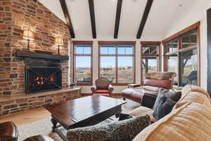 Living room with large view windows, light oak floors, a stone gas fireplace, beamed ceiling, and a high vaulted ceiling