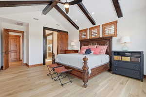 Primary bedroom suite with a barn door, light oak floors, vaulted beam ceiling, large view windows and door to covered deck