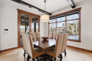 Dining area featuring light oak flooring, beamed ceiling, door to the covered deck and large view windows with plenty of natural light