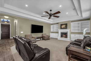 Living room featuring a tray ceiling, a glass covered fireplace, recessed lighting, ceiling fan, and arched walkways