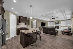 Kitchen featuring dark brown cabinets, decorative light fixtures, a kitchen bar, a raised ceiling, and open floor plan