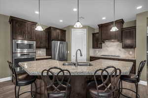 Kitchen featuring dark brown cabinetry, dark wood finished floors, hanging light fixtures, appliances with stainless steel finishes, and backsplash