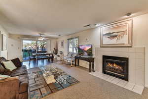 Living area featuring carpet floors, a tile fireplace, healthy amount of natural light, a textured ceiling, and a ceiling fan