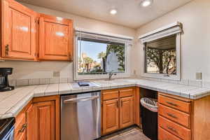 Kitchen with tile countertops, stainless steel dishwasher, brown cabinets, a textured ceiling, and recessed lighting