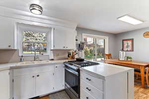 Kitchen with stainless steel range with gas stovetop, a peninsula, light countertops, and white cabinetry