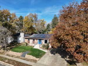 View of front facade with solar panels, a front yard, and a chimney