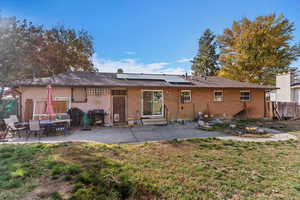 Rear view of house featuring a patio, solar panels, brick siding, and a shingled roof