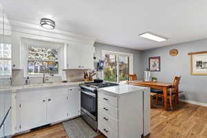 Kitchen featuring stainless steel gas range, light countertops, a peninsula, white cabinets, and light wood-type flooring