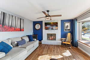 Living area featuring wood finished floors, a fireplace, a ceiling fan, and an accent wall