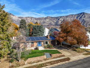 View of front of home with roof mounted solar panels, driveway, a mountain view, a chimney, and a front yard