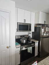 Kitchen with stainless steel appliances, white cabinets, dark wood-style flooring, light stone countertops, and a textured ceiling