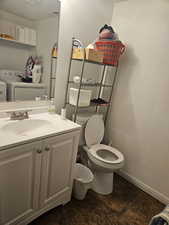 Half bath with a textured wall, vanity, and washing machine and clothes dryer