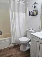 Bathroom featuring a textured wall, vanity, shower / bathtub combination with curtain, and dark wood-style flooring