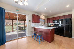 Kitchen featuring black appliances, light countertops, a breakfast bar, reddish brown cabinets, and light wood-style floors