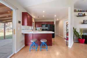 Kitchen with light countertops, dark brown cabinets, black appliances, a peninsula, and light wood-style flooring