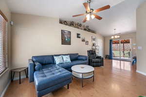 Living area with a chandelier, light wood-style flooring, ceiling fan, and lofted ceiling