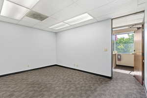 Carpeted spare room featuring baseboards and a drop ceiling