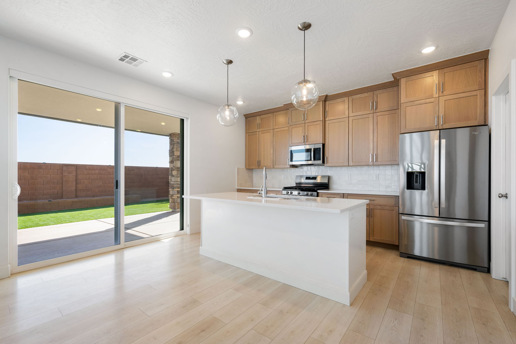 Kitchen with appliances with stainless steel finishes, tasteful backsplash, light stone counters, decorative light fixtures, and an island with sink