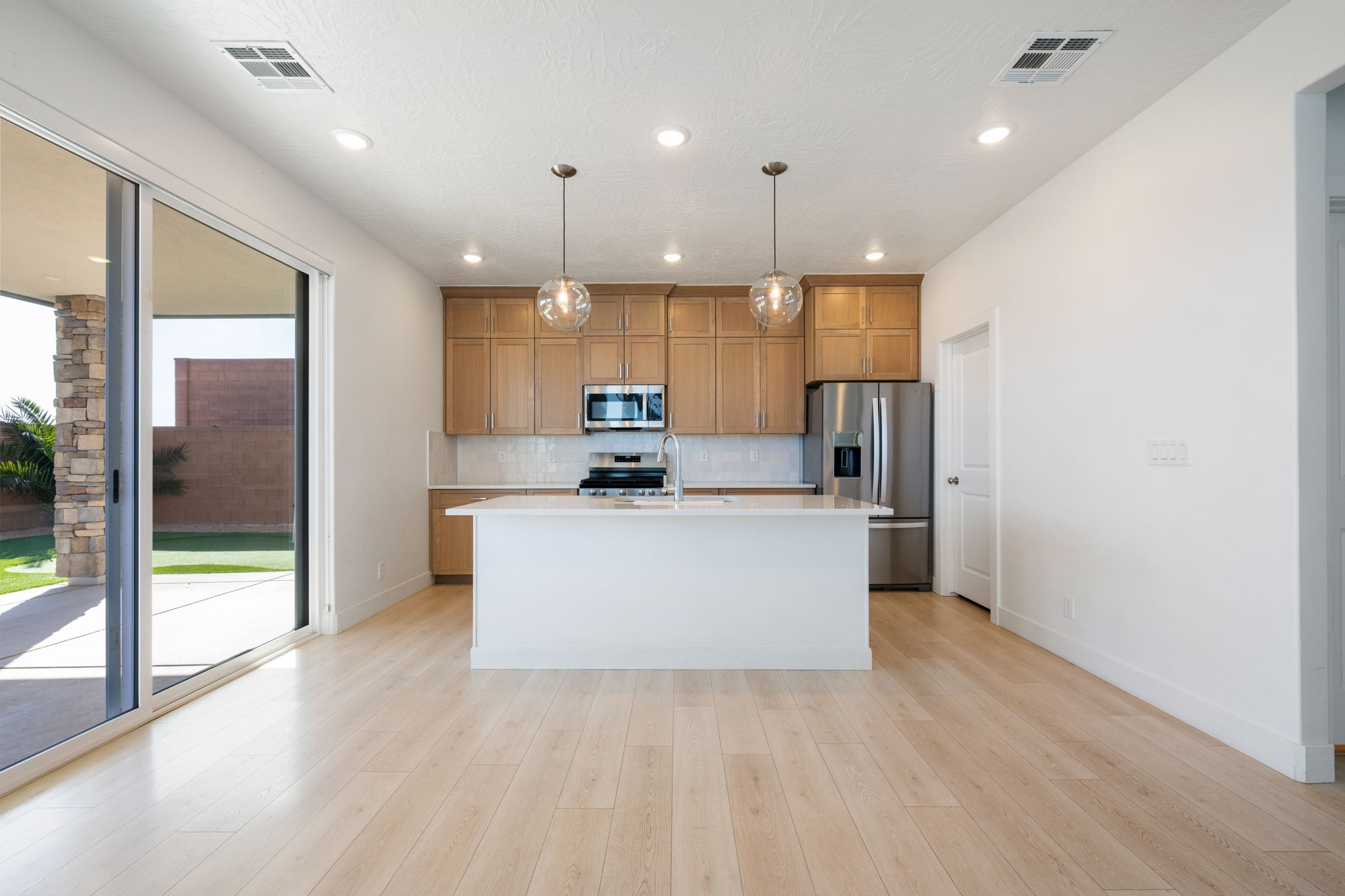 Kitchen with stainless steel appliances, an island with sink, brown cabinetry, decorative light fixtures, and light wood-style flooring