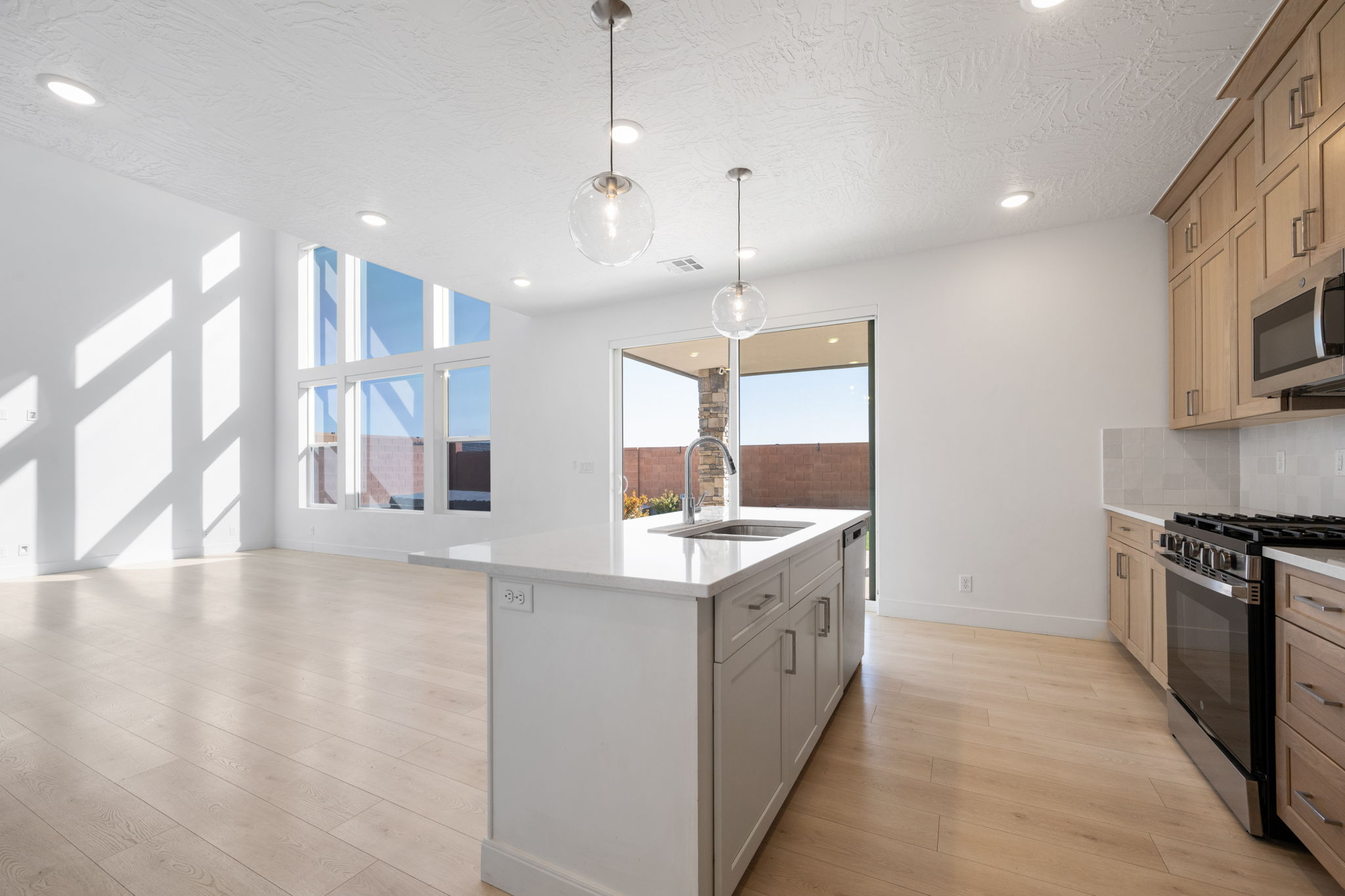 Kitchen with appliances with stainless steel finishes, pendant lighting, light stone countertops, a kitchen island with sink, and light wood-style floors