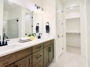 Bathroom with double vanity, a walk in closet, a shower stall, and light tile patterned floors