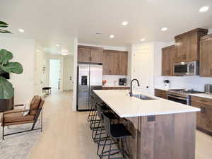 Kitchen with stainless steel appliances, a kitchen breakfast bar, a kitchen island with sink, light wood-style floors, and recessed lighting