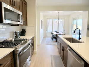 Kitchen featuring stainless steel appliances, light wood-style floors, tasteful backsplash, light stone countertops, and hanging lights