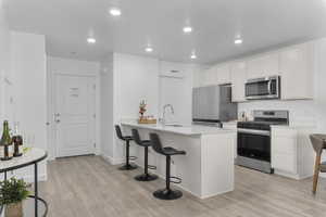 Kitchen with a breakfast bar, appliances with stainless steel finishes, a peninsula, white cabinets, and light wood-type flooring