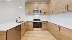 Kitchen featuring light wood finish cabinets, stainless steel appliances, decorative light fixtures, and a peninsula