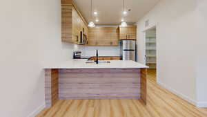 Kitchen with stainless steel appliances, light wood-style floors, light wood finish cabinetry, hanging light fixtures, and a peninsula