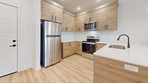 Kitchen with stainless steel appliances, light wood finish cabinetry, modern cabinets, light stone counters, and recessed lighting