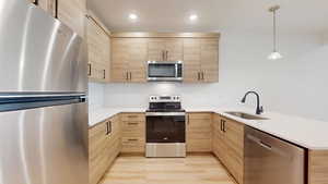 Kitchen with stainless steel appliances, light wood finish cabinets, and pendant lighting