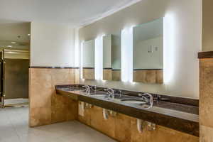 Bathroom featuring light tile patterned floors, double vanity, tile walls, recessed lighting, and wainscoting