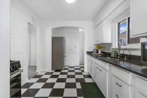 Kitchen with dark floors, white cabinets, freestanding refrigerator, dark stone countertops, and range