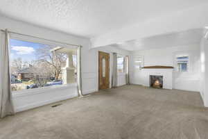 Unfurnished living room featuring carpet, a brick fireplace, and a textured ceiling
