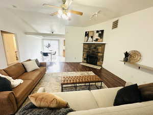 Living room featuring wood finished floors, a stone fireplace, lofted ceiling, a ceiling fan, and rail lighting