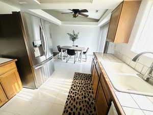 Kitchen featuring tile counters, stainless steel fridge, a ceiling fan, brown cabinets, and light tile patterned floors