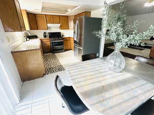 Kitchen featuring tile countertops, stainless steel appliances, brown cabinets, and under cabinet range hood