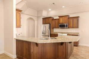 Kitchen featuring brown cabinetry, stainless steel appliances, a peninsula, light stone counters, and a kitchen breakfast bar