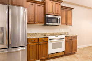 Kitchen featuring appliances with stainless steel finishes, light stone countertops, brown cabinets, and light tile patterned floors