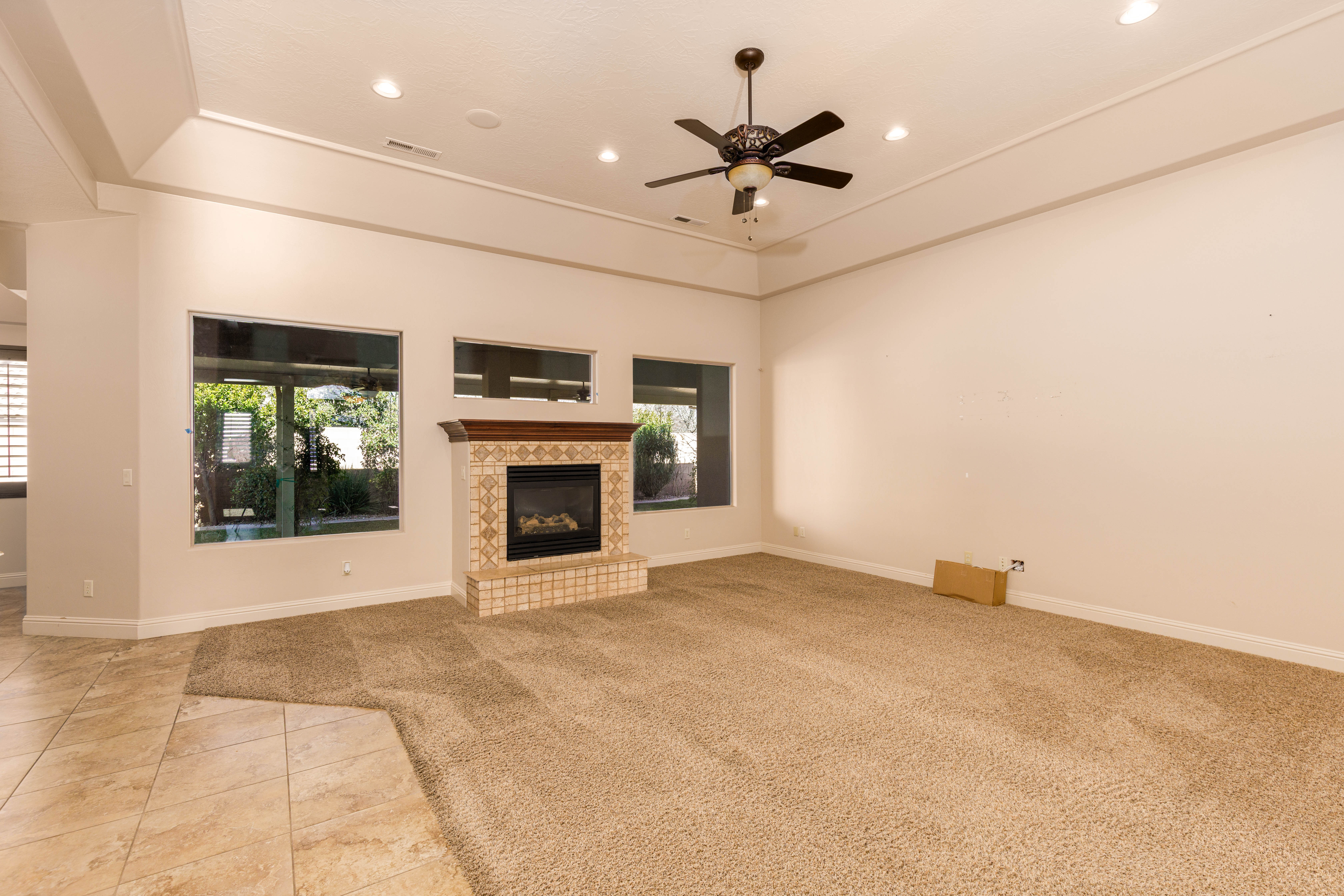 Unfurnished living room featuring light carpet, a fireplace, a ceiling fan, a raised ceiling, and recessed lighting