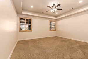 Carpeted empty room with healthy amount of natural light, a ceiling fan, a tray ceiling, and recessed lighting