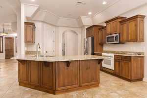 Kitchen with a breakfast bar, light stone counters, brown cabinetry, a peninsula, and stainless steel appliances