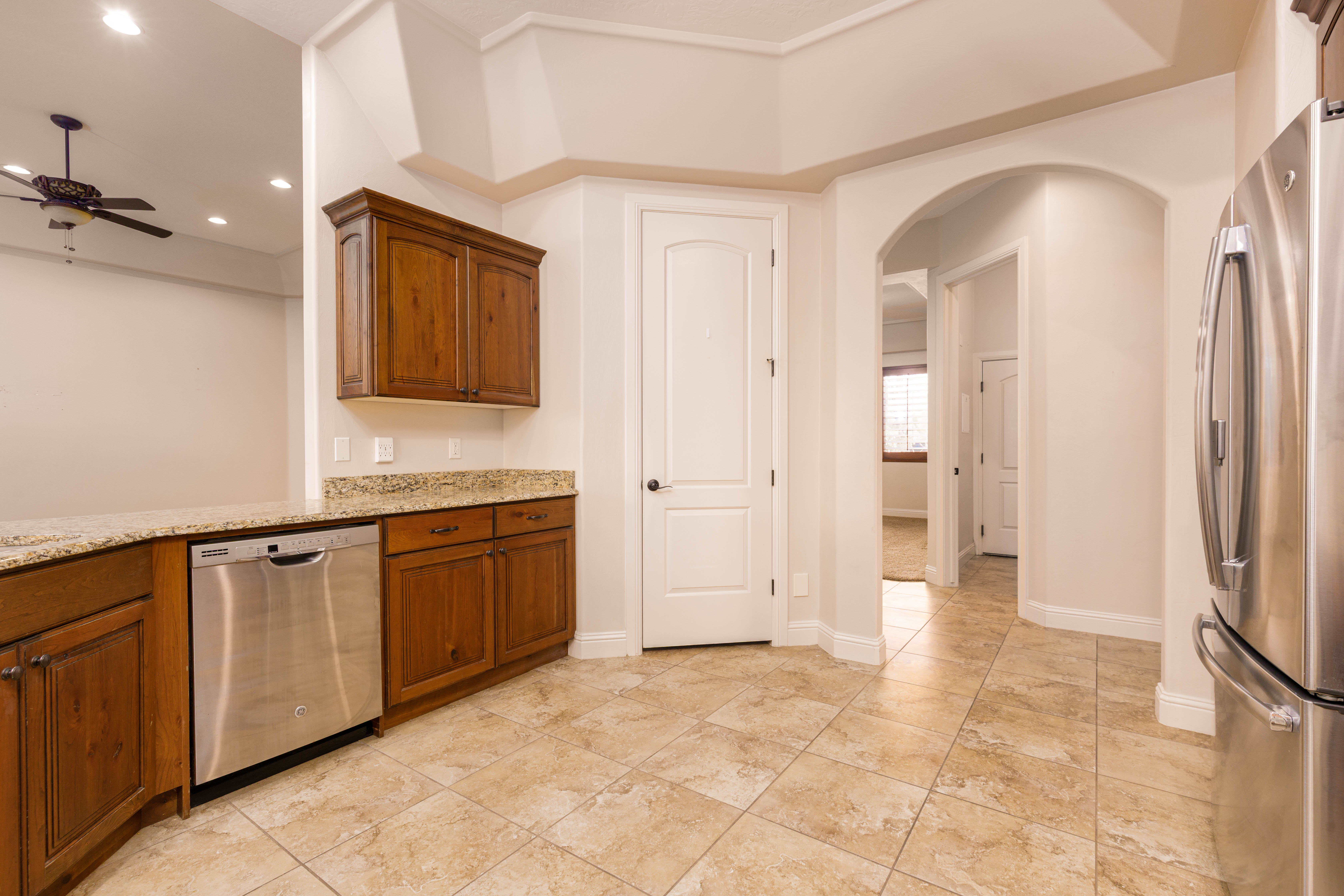 Kitchen featuring light stone countertops, appliances with stainless steel finishes, arched walkways, ceiling fan, and brown cabinets