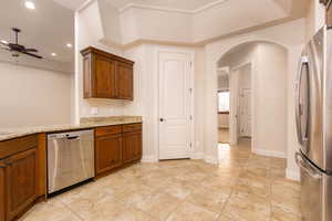 Kitchen featuring light stone countertops, appliances with stainless steel finishes, arched walkways, ceiling fan, and brown cabinets