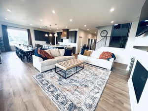 Living room featuring stairs, light wood-style flooring, recessed lighting, and a glass covered fireplace