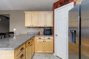 Kitchen with stainless steel refrigerator with ice dispenser, a peninsula, a textured ceiling, light brown cabinetry, and dark countertops