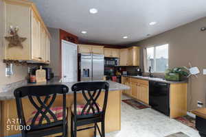 Kitchen featuring black appliances, light brown cabinetry, a breakfast bar area, a peninsula, and recessed lighting